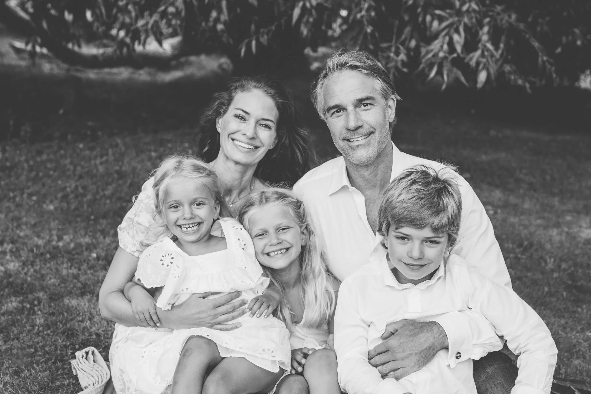familj som sitter i gräset. mamma, pappa, och tre barn som skrattar. bilden är svartvit