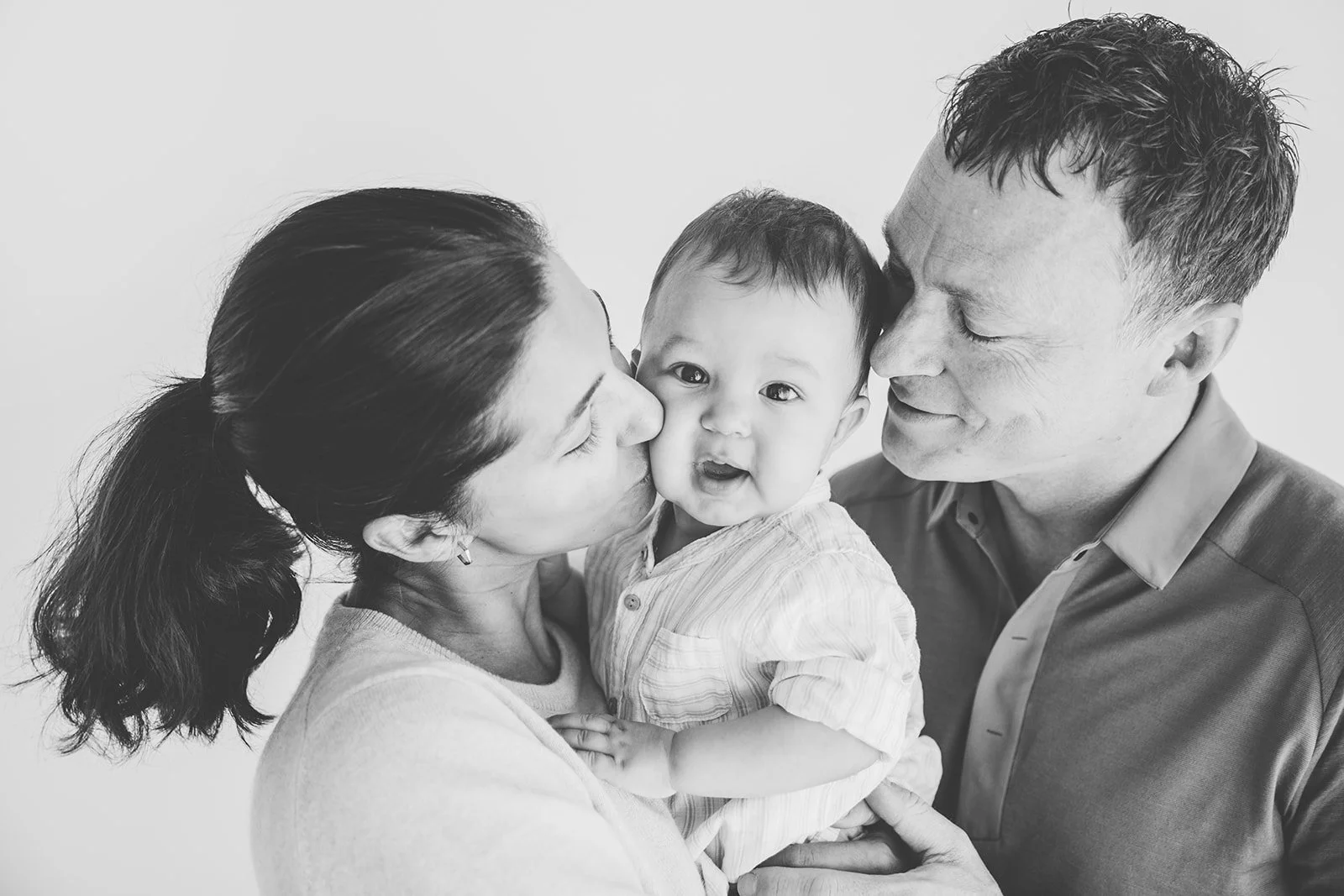 Mamma och pappa pussar sin lilla son under en familjefotografering i studio.