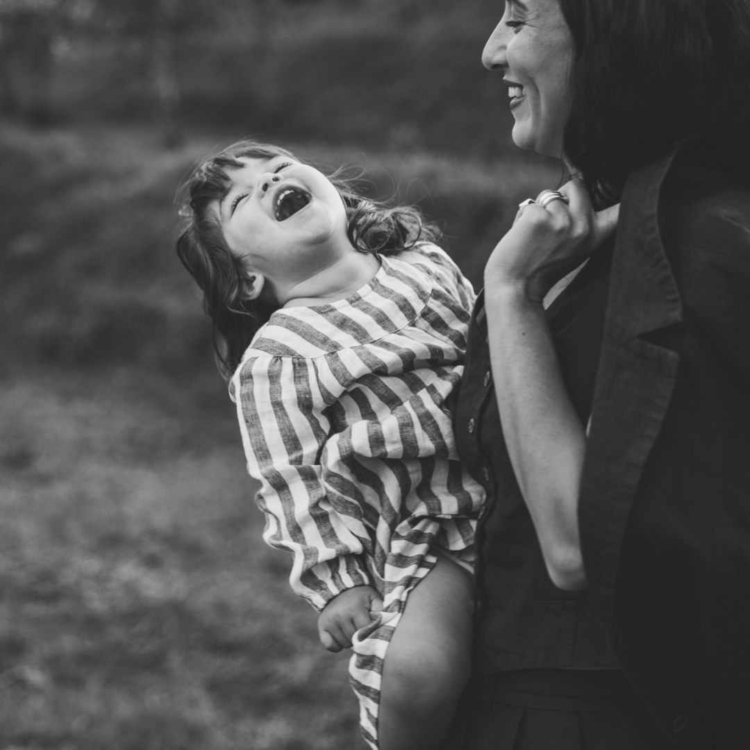 mamma håller upp sin dotter och snurrar runt. båda skrattar.