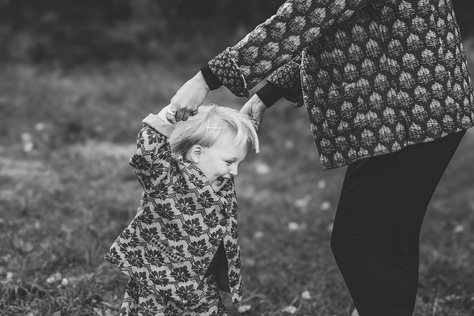 barn som håller mamma i händerna och dansar på en äng. båda har mönstrade kläder