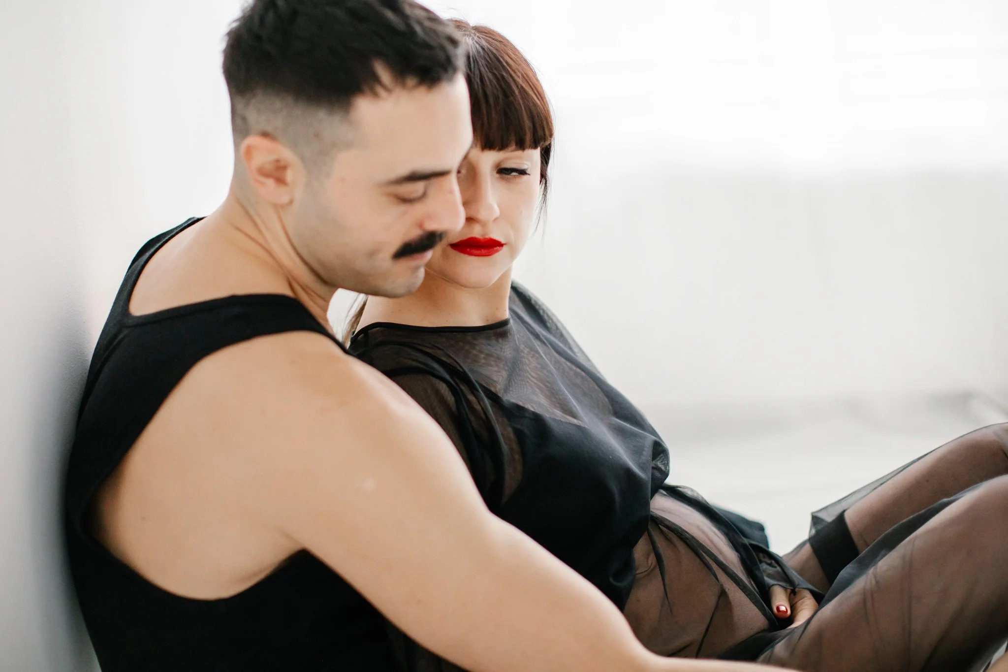 En kvinna och man sitter mot en vägg. Båda har svarta kläder.