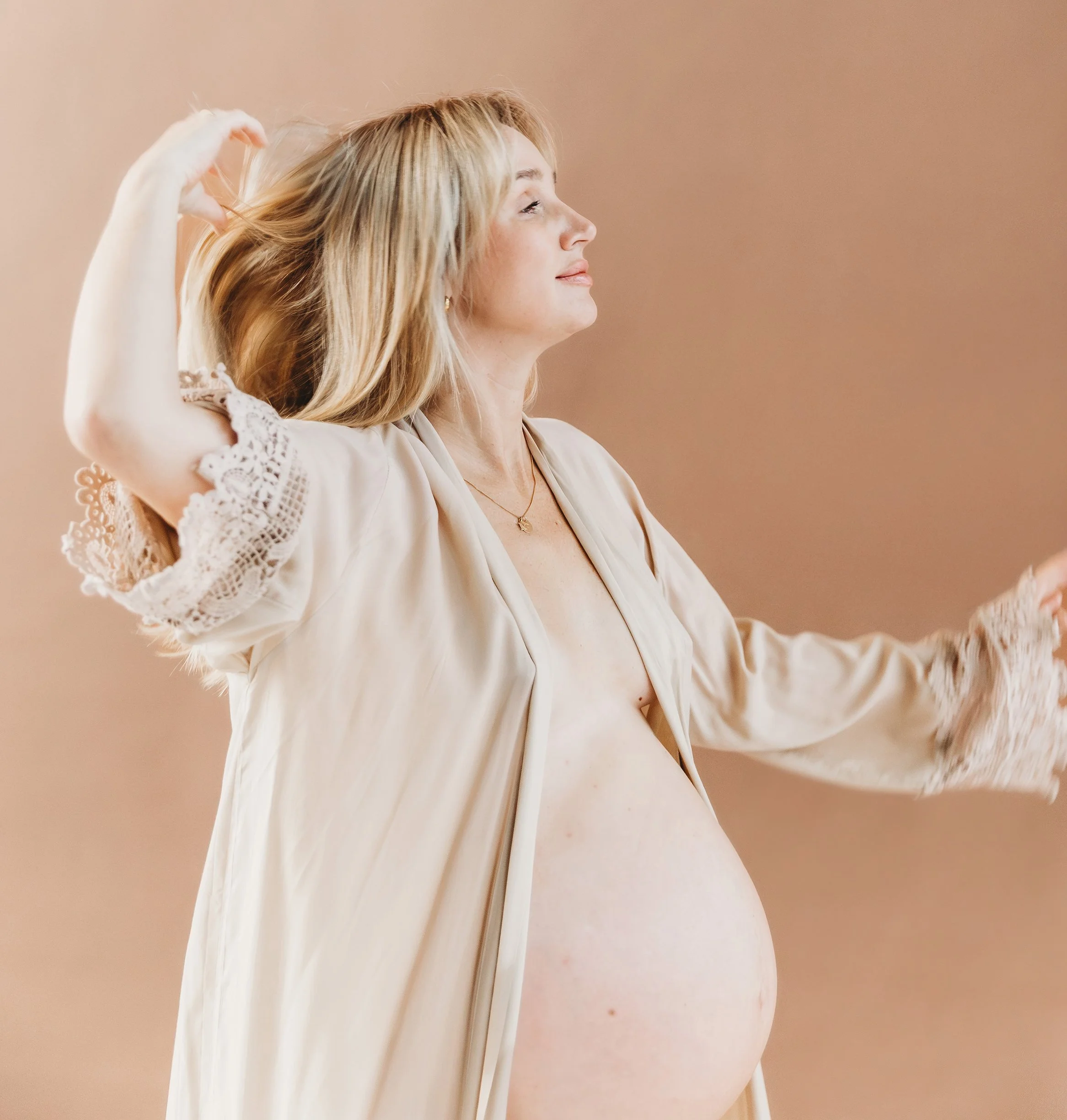 gravid kvinna som visar magen i en beige kimono. hon slänger med sitt blonda hår.