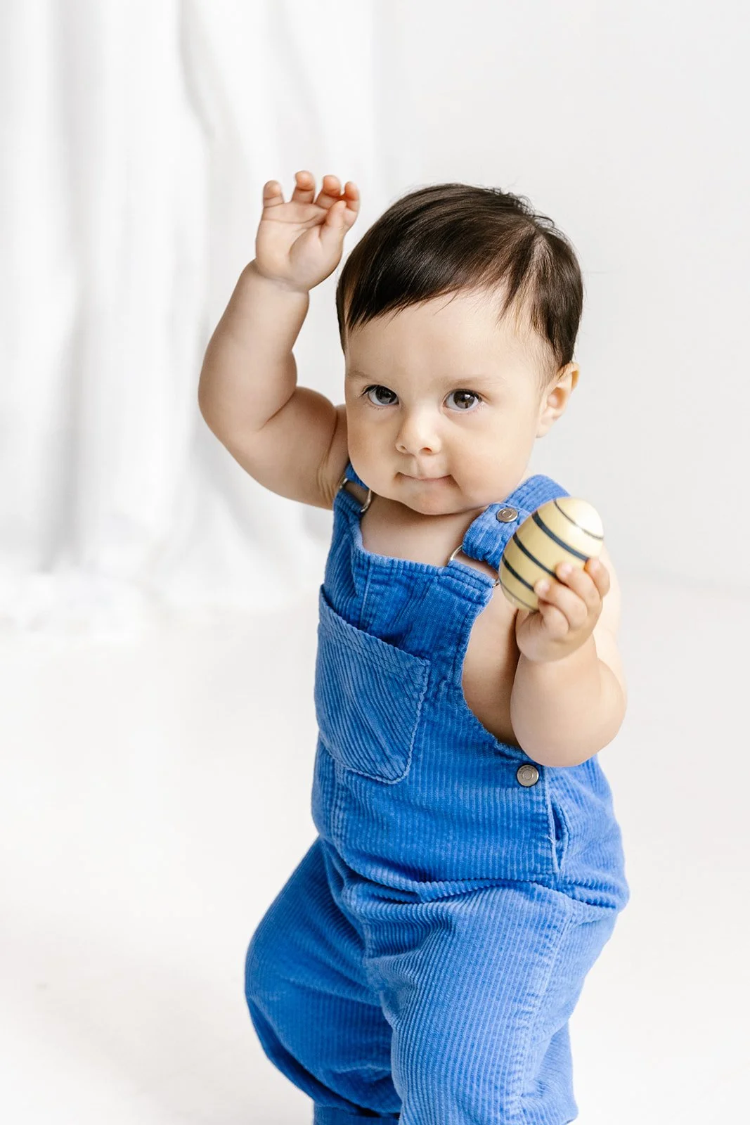 Liten pojke med blå hängselbyxor dansar i en fotostudio.
