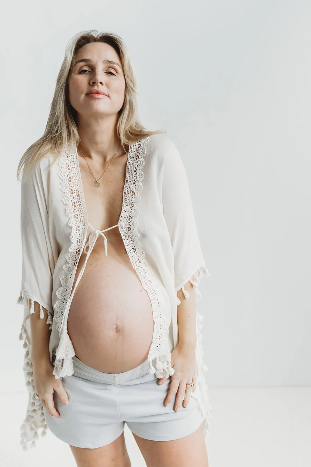 Gravid blond kvinna fotad mot vit bakgrund i studio. Kvinnan har en beige kimono.