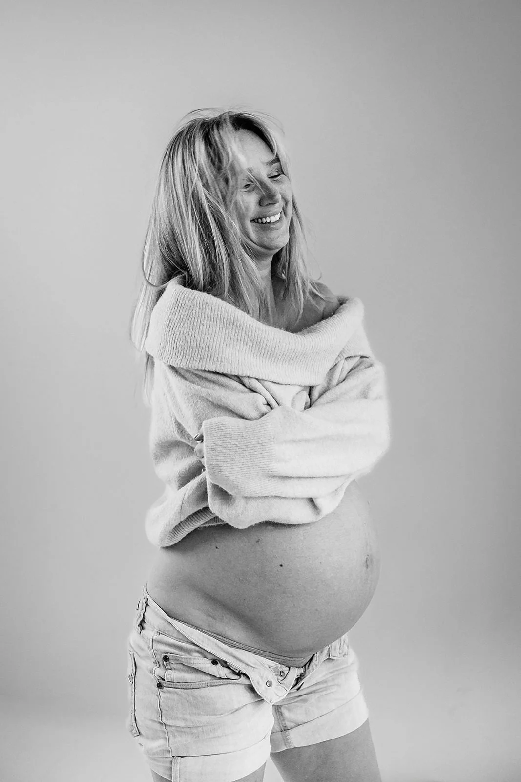 Gravid kvinna som skrattar och har en stickad tröja på sig.