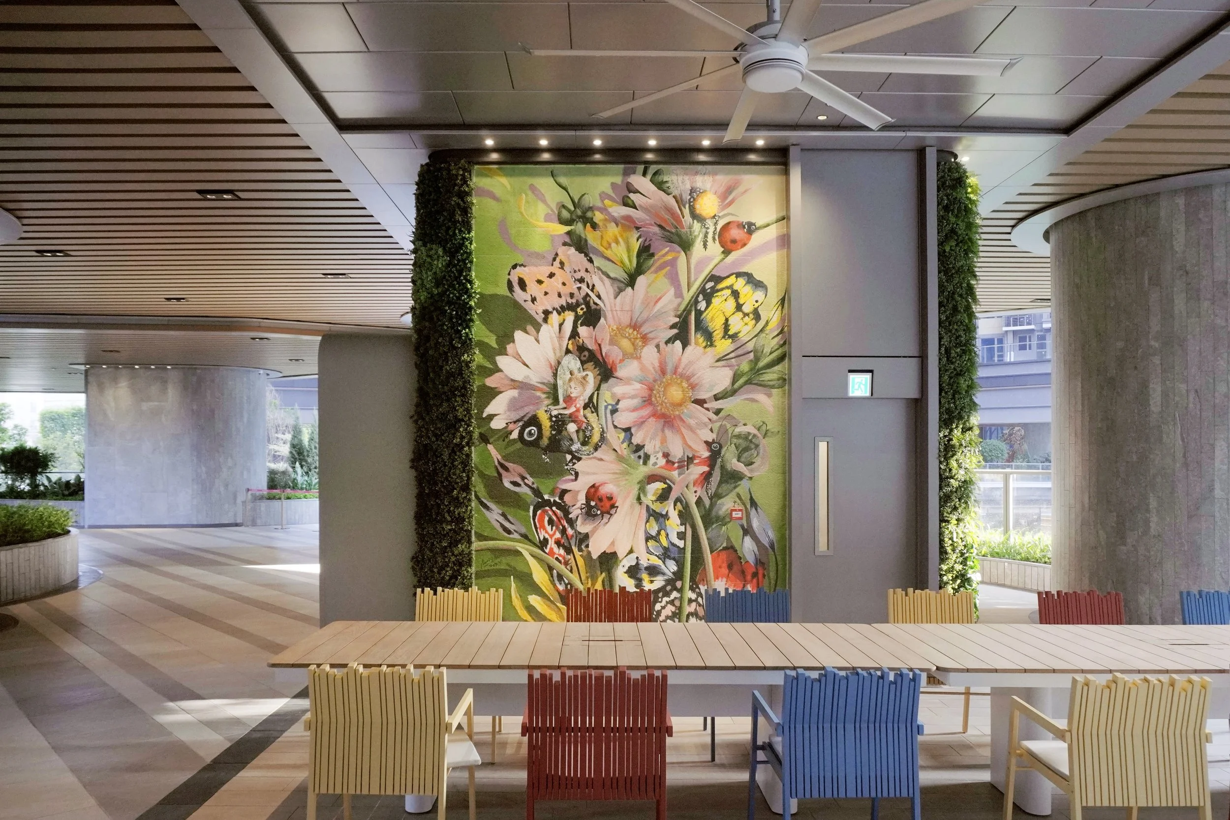 Residential estate mural created and painted by artist Neil Wang featuring bright colored nature plants, flowers, bold and whimsical ladybirds and butterflies, in the social zone in Novoland Hong Kong by Sun Hung Kai Properties.