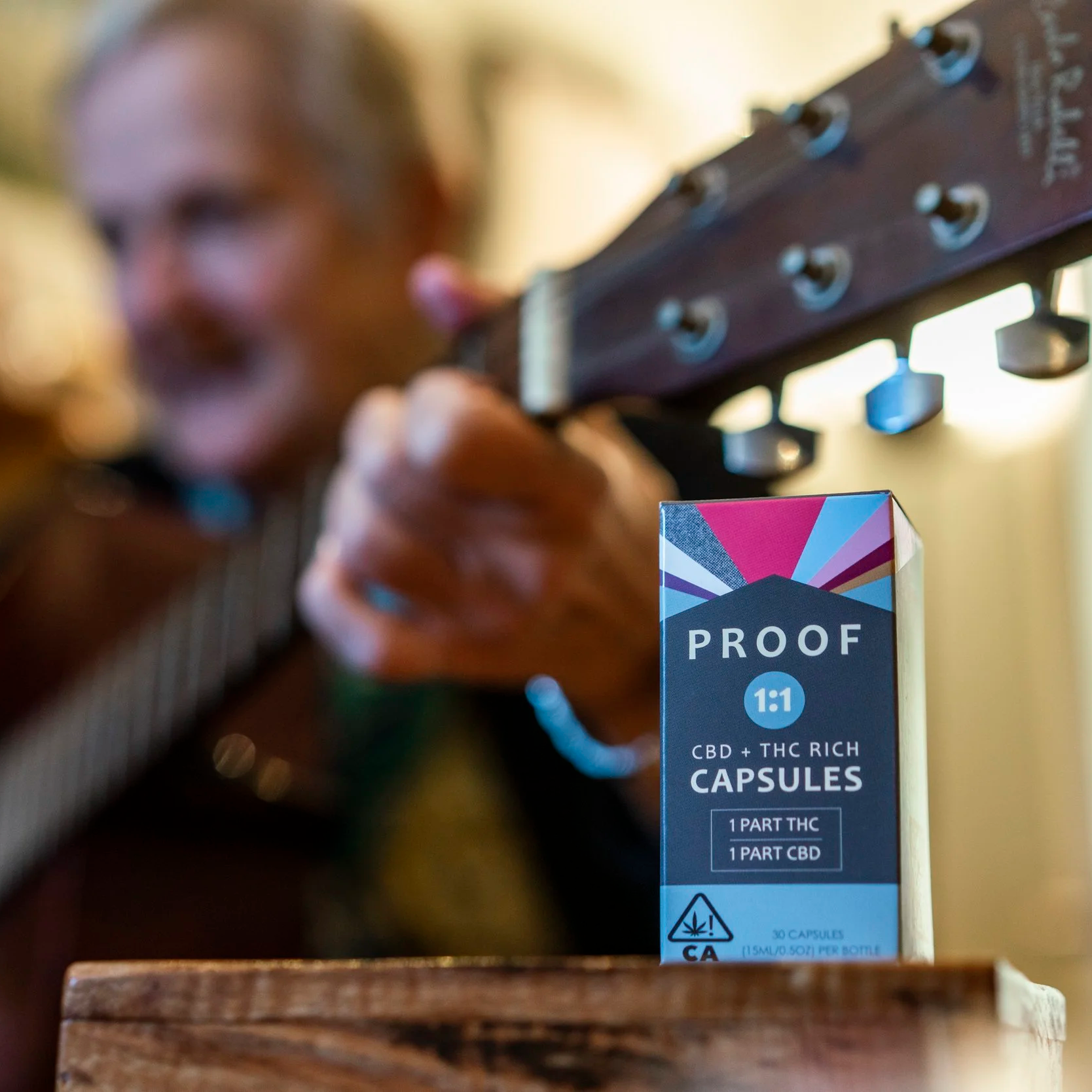 Older woman playing guitar with Proof 1:1 capsules in the foreground