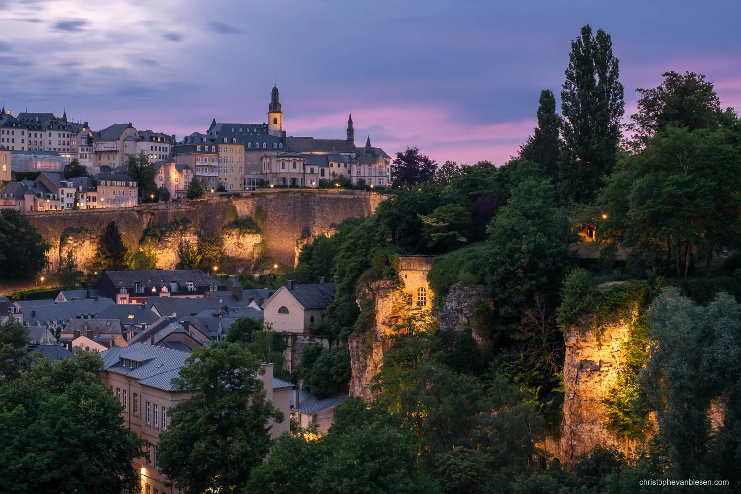 Luxembourg’s Grund and illuminated fortifications beneath a purple sky, with Saint Michael’s Church above.
