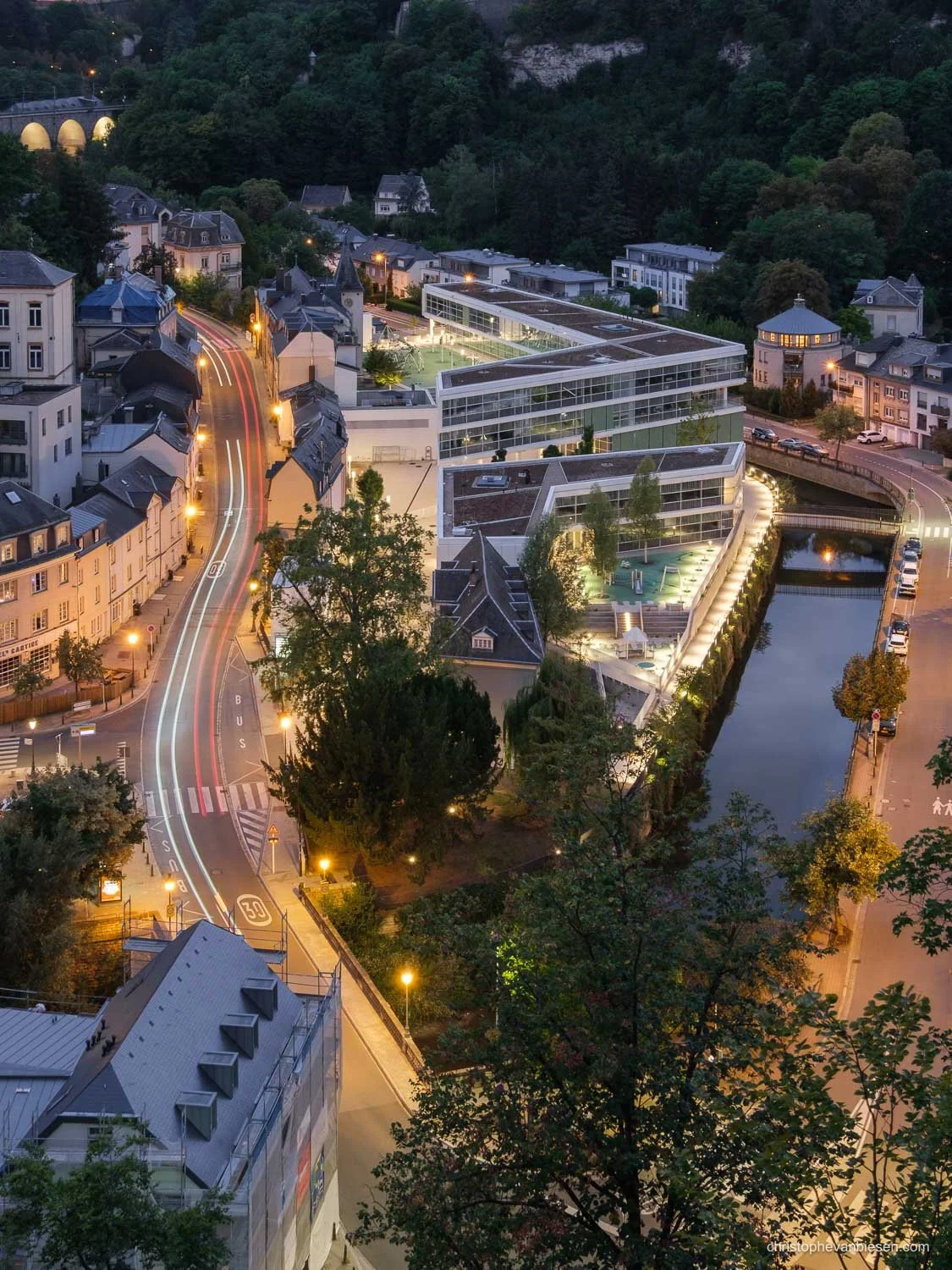 Light trails through Clausen in Luxembourg City, beside contemporary buildings and the Alzette river.