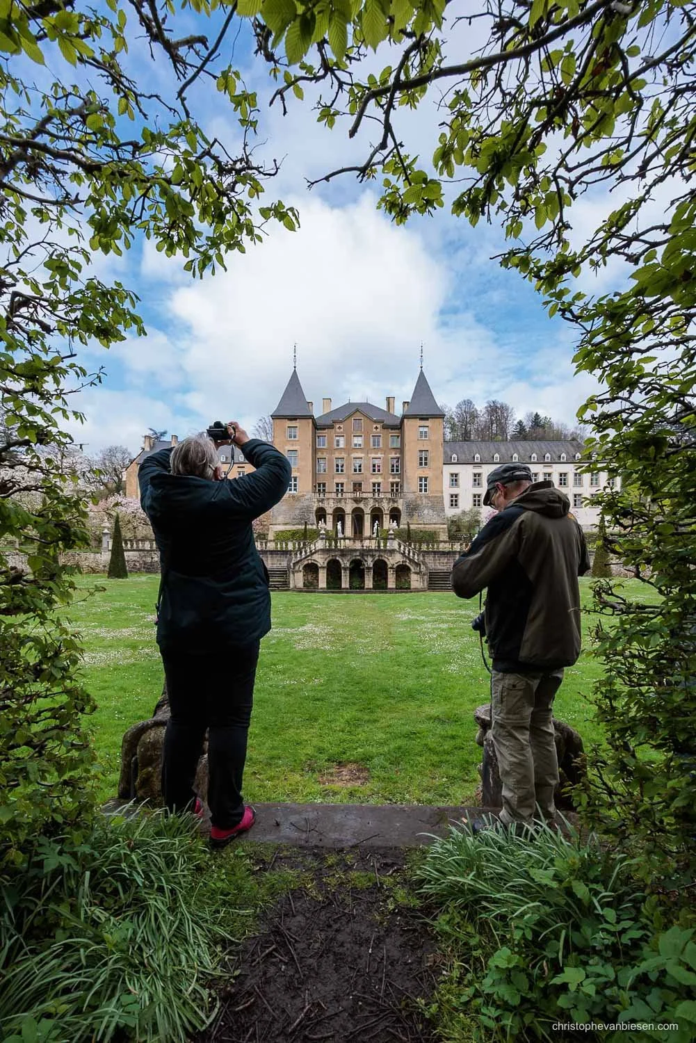 Two photographers framing a castle through leafy branches in its gardens.
