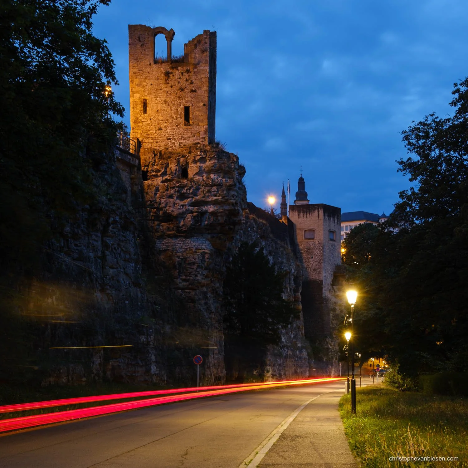 The illuminated Hollow Tooth tower in Luxembourg City, with red light trails beneath a blue sky.