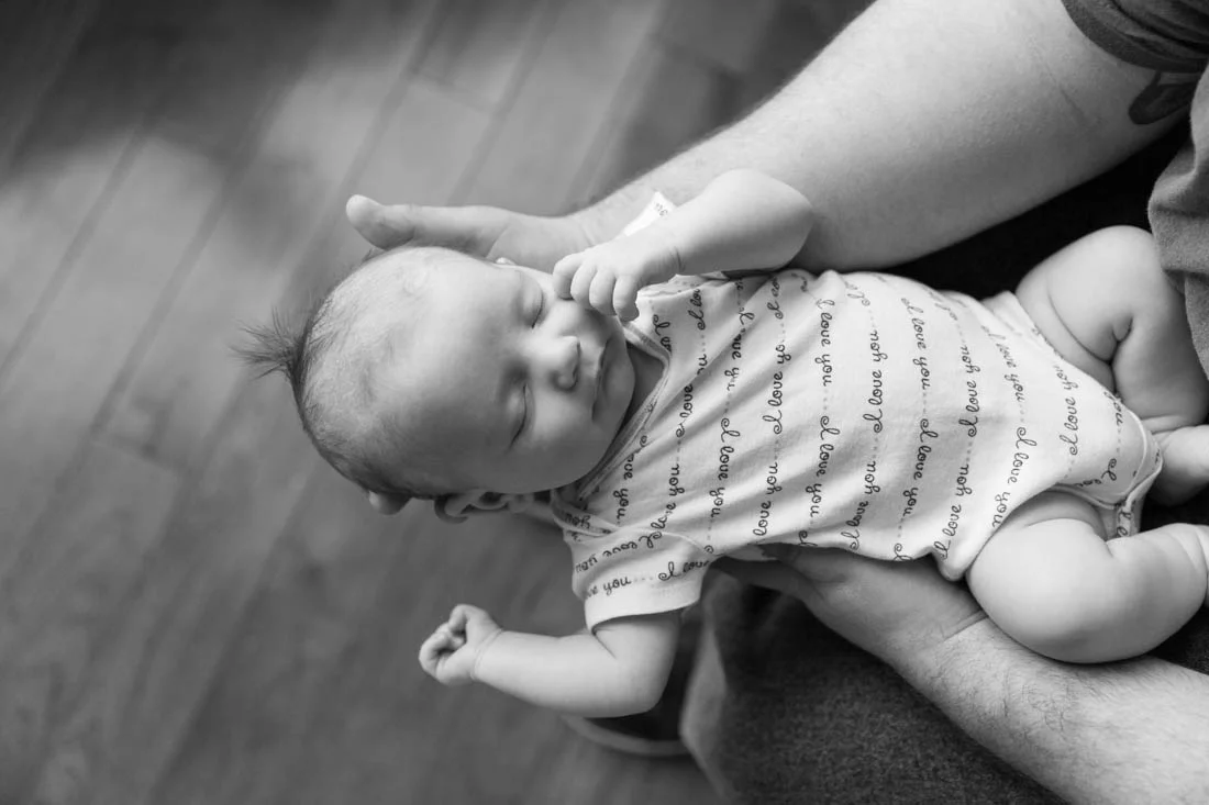 Newborn baby girl sleeping in her father’s arms during a newborn in home session