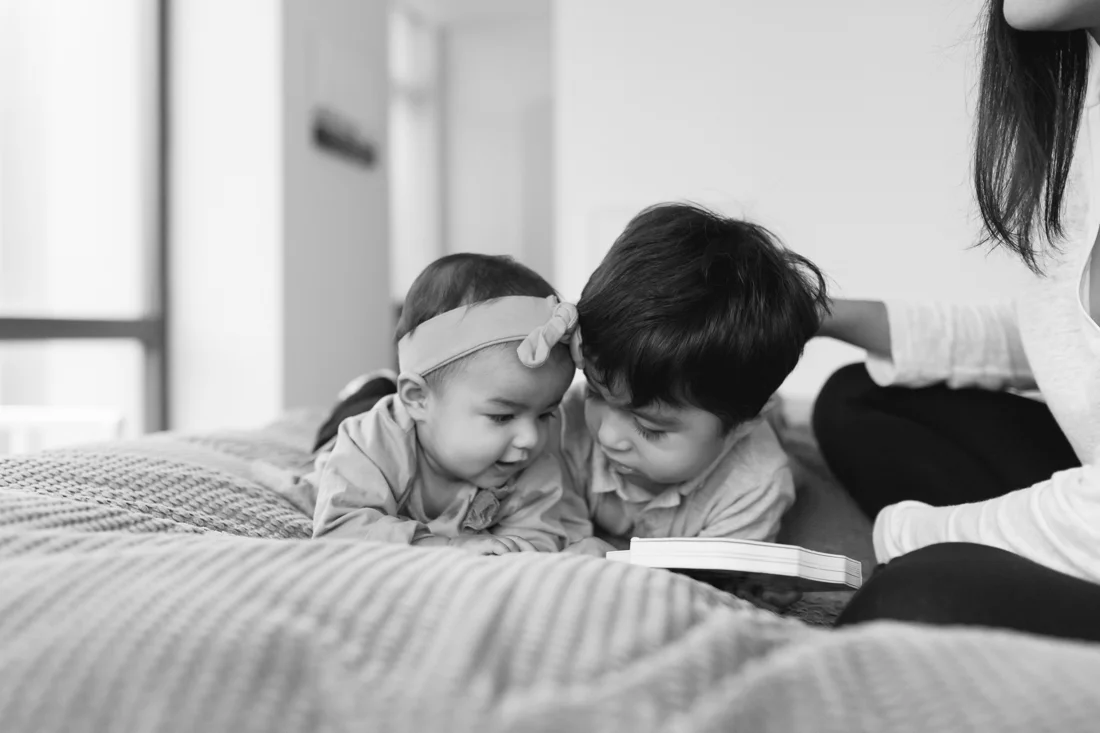 Siblings reading a book together on parents bed during a manhattan family session at home