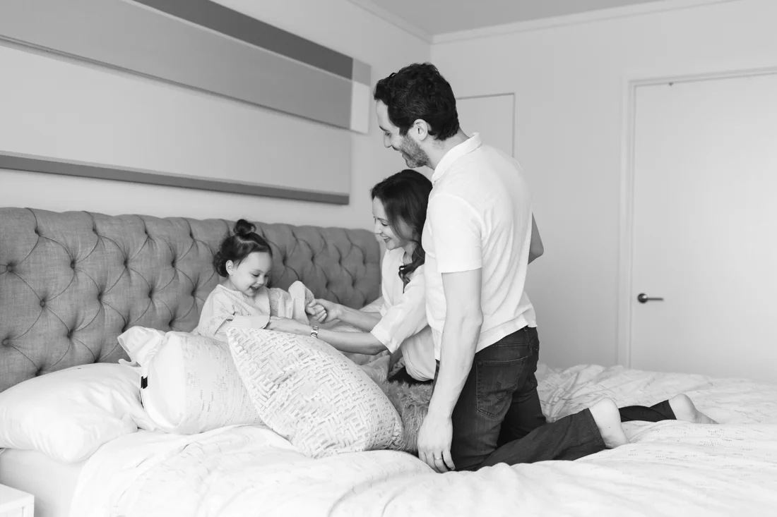 Parents and toddler playing in bed during in home photo session