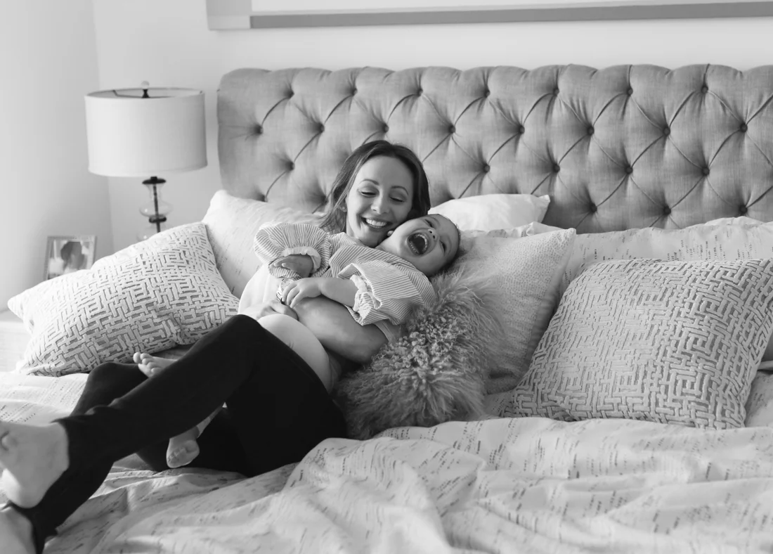 Mother and two years old daughter laughing on bed during a photo session at home