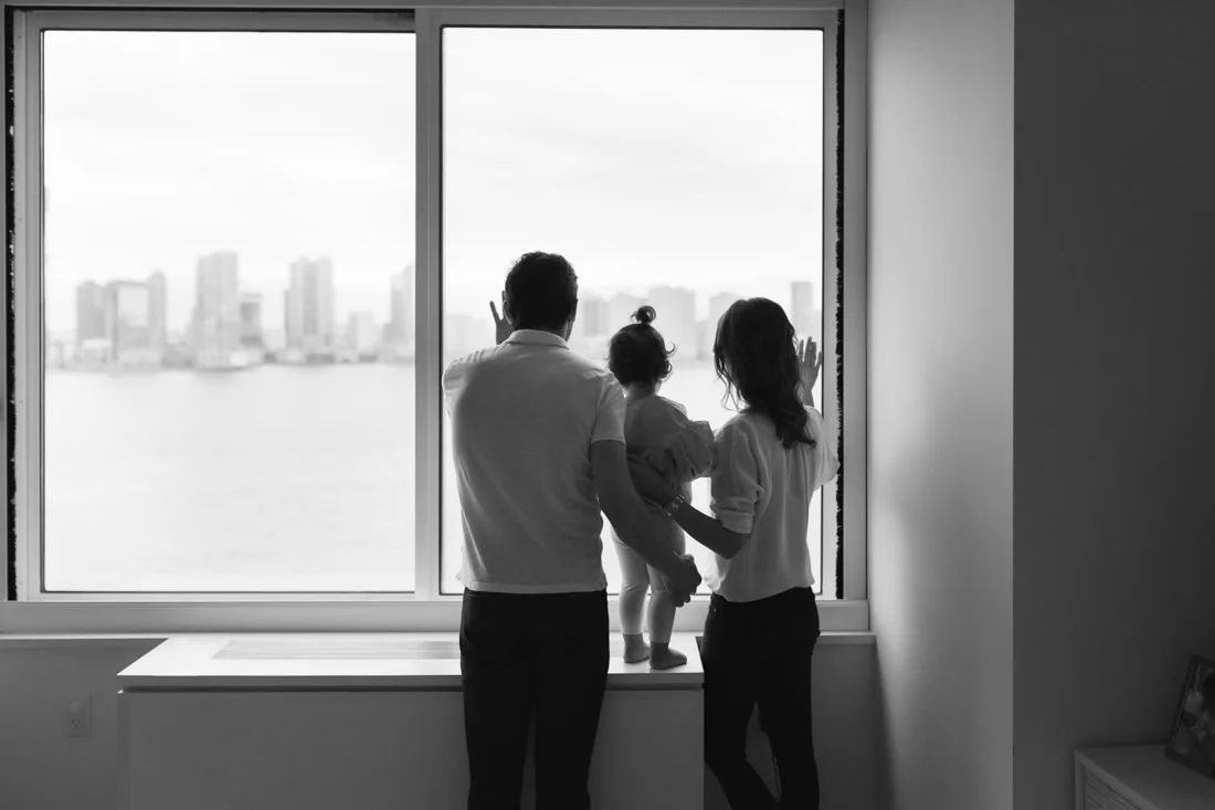 Parents and toddler looking outside the window with city view