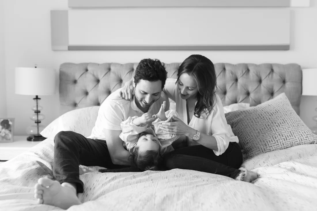 Parents hugging and playing with toddler on bed during an in-home family session