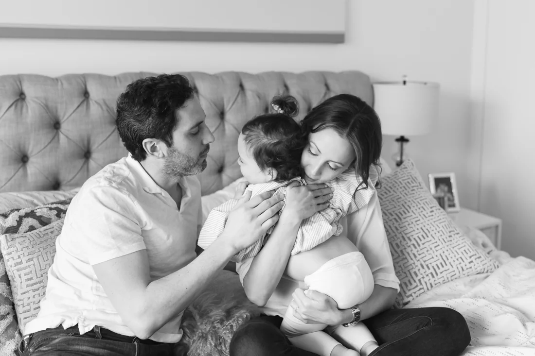 Parents hugging toddler on bed during an in-home family session