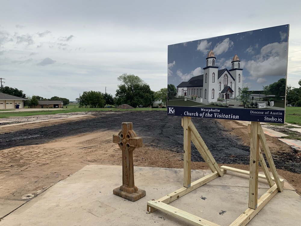  A salvaged cross and rendering of the new church  in front of a site that bears ashes as the only trace of what previously stood here. 