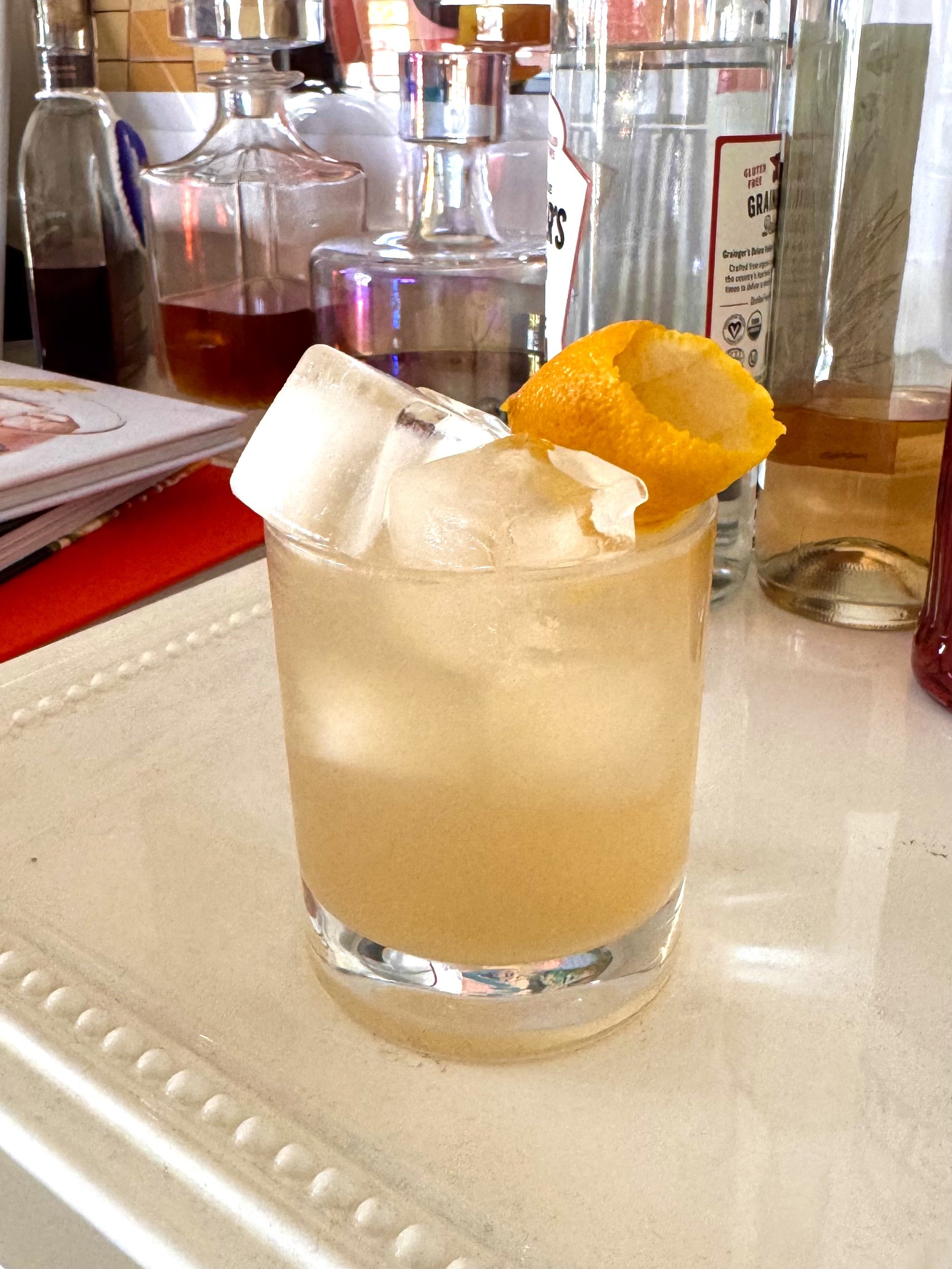 Light yellow drink with square ice cubes and a lemon twist