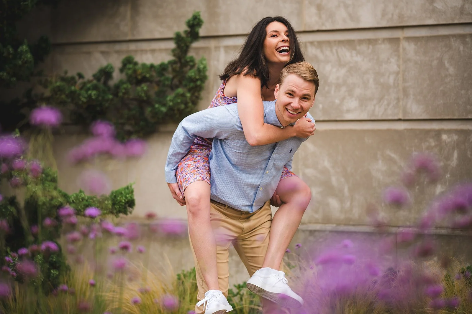 Engaged couple laughing during a piggyback ride among purple flowers near the U.S. Botanic Garden in Washington, D.C., photographed by Gabriele Stonyte Photography