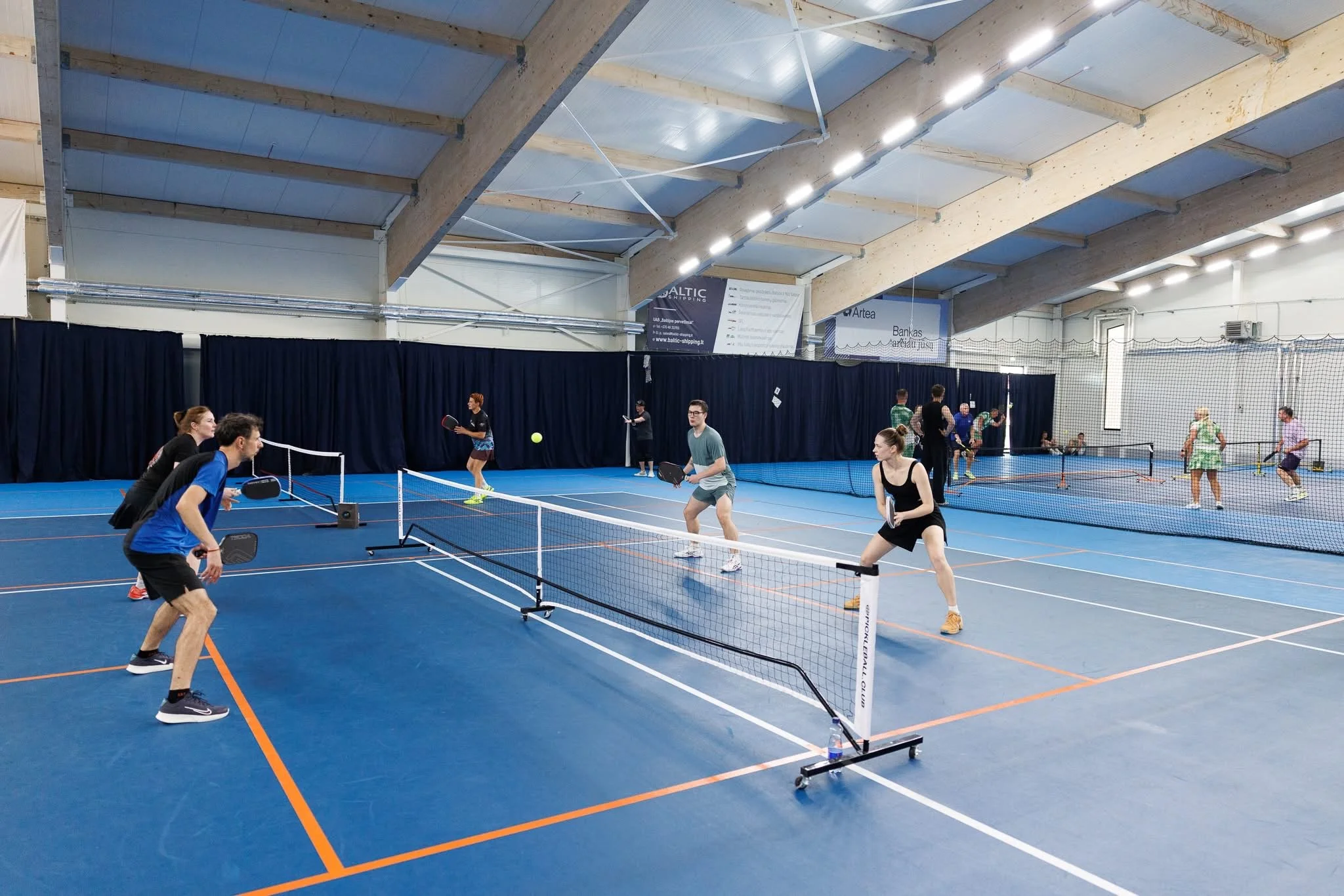 People playing pickleball on an indoor court with blue flooring and multiple courts.
