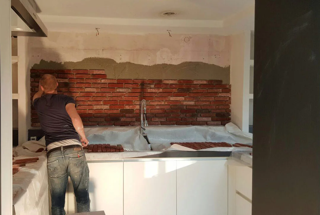 Een man aan het werk met het plaatsen van bakstenen achter een keukenkastje.