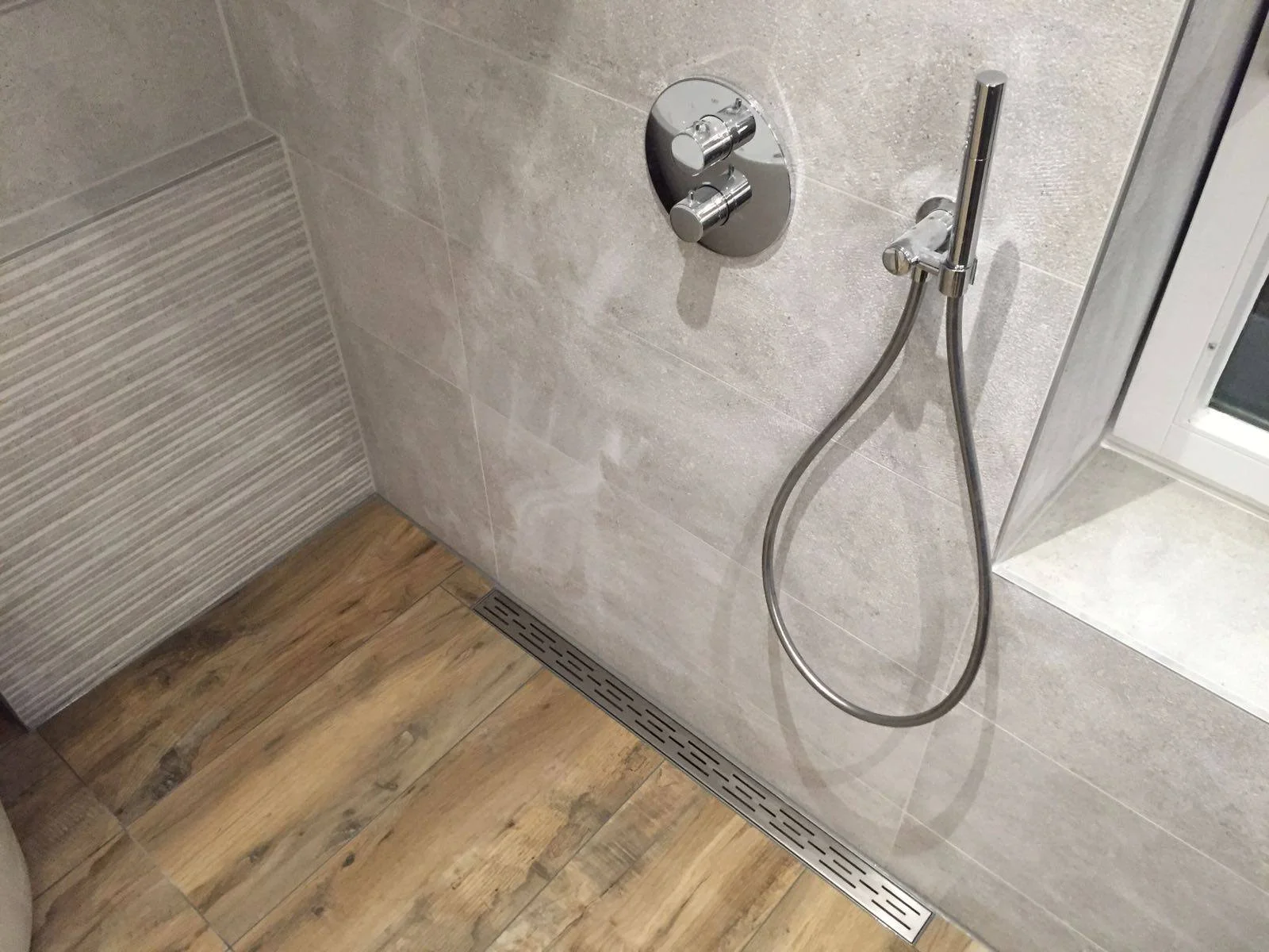 Douche met een handdouche en een bedieningsknop aan de muur, met een regenwaterafvoer op de vloer.