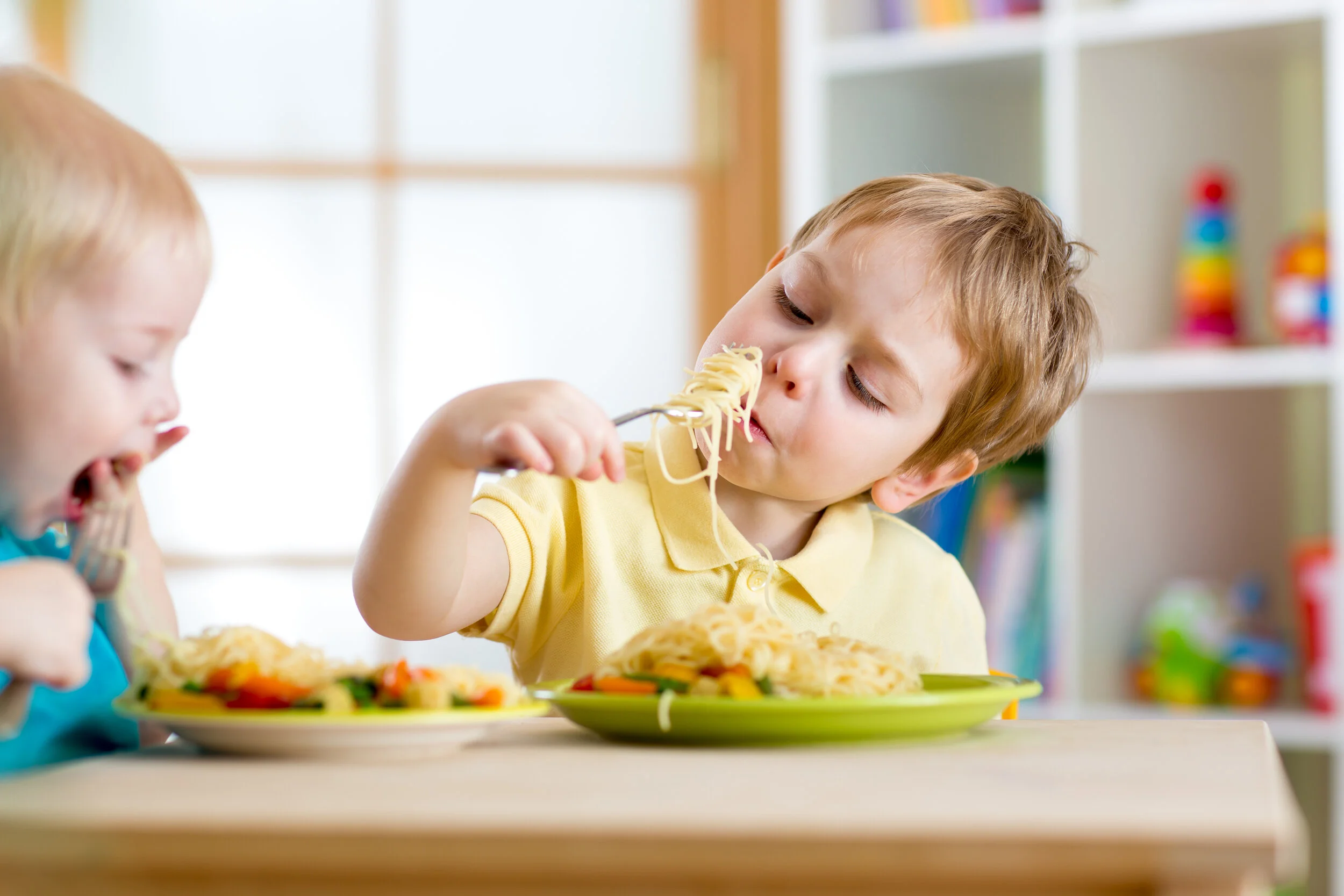 Toddler boys eating spaghetti with a fork