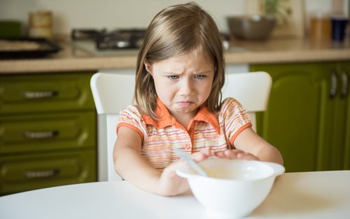 young girl pushing bowl of food away from her