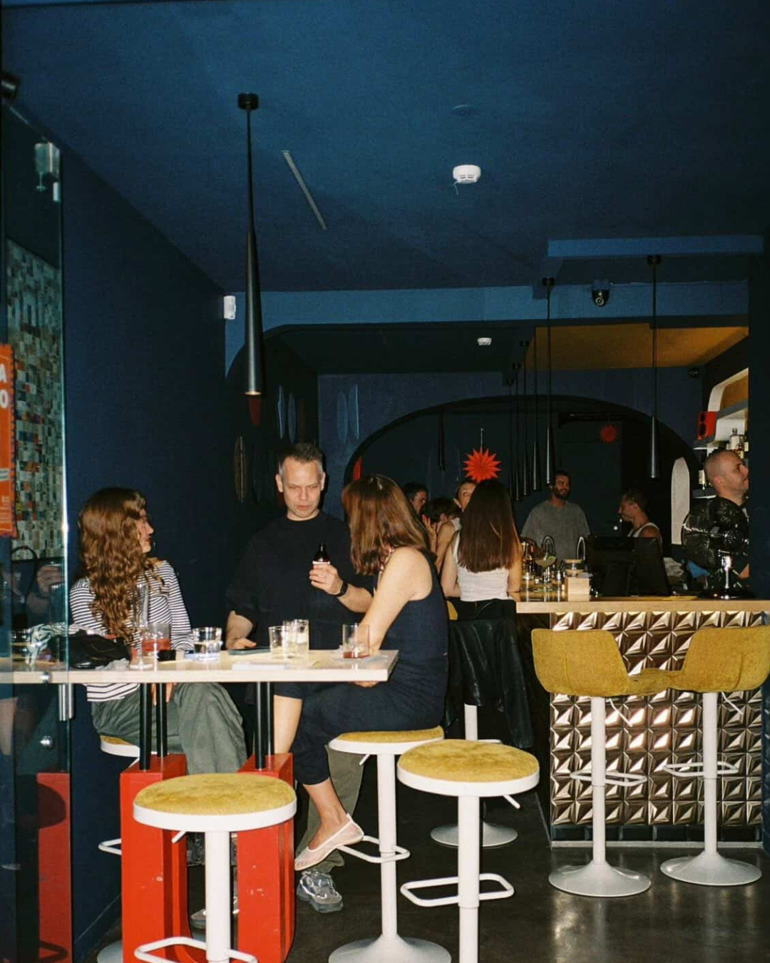 Busy evening at Agência Bar Lisbon with deep blue interiors, retro bar stools and a lively crowd at the counter