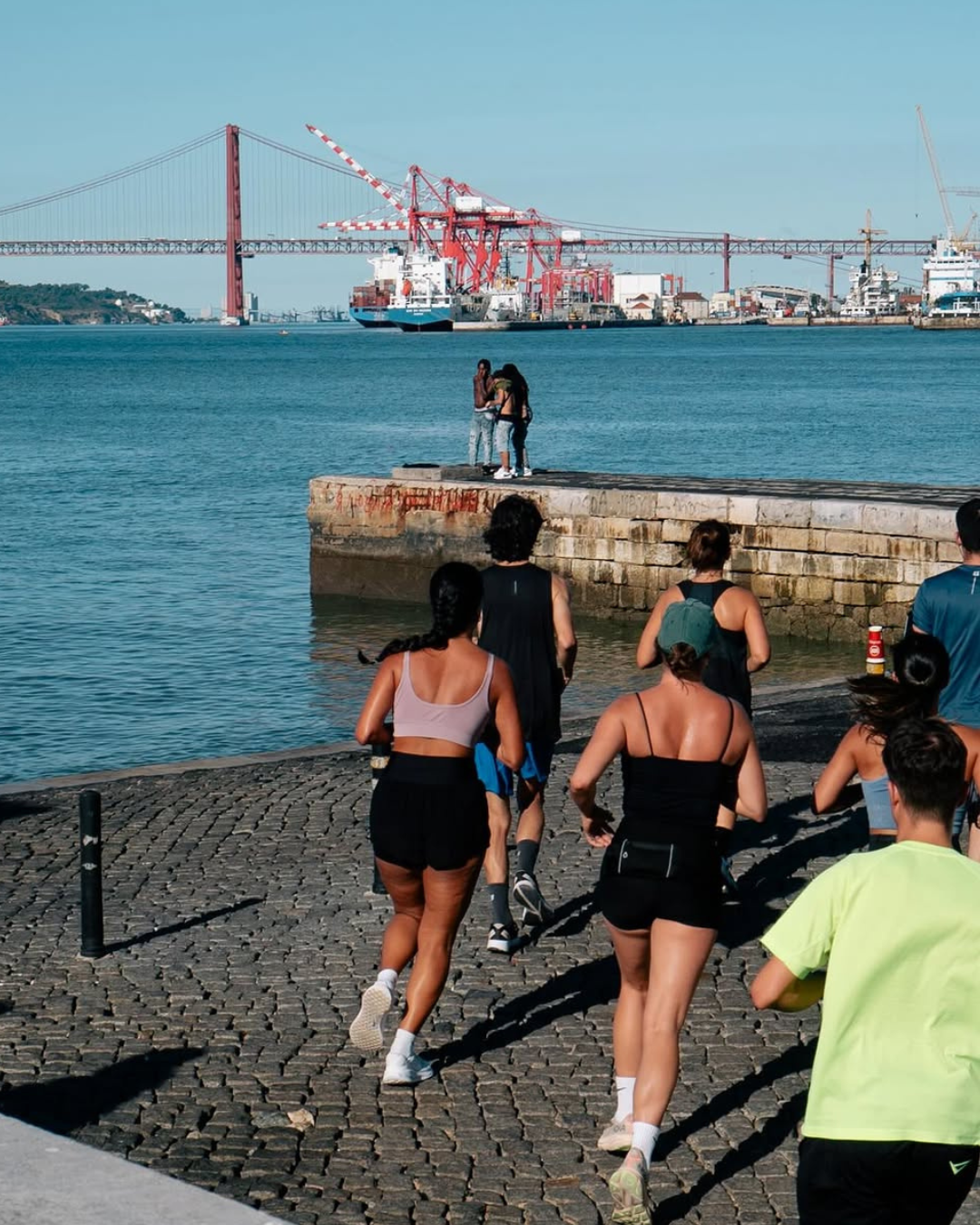Group of runners along the Tagus riverfront with the Ponte 25 de Abril bridge in the background, Rookie Run Club Lisbon