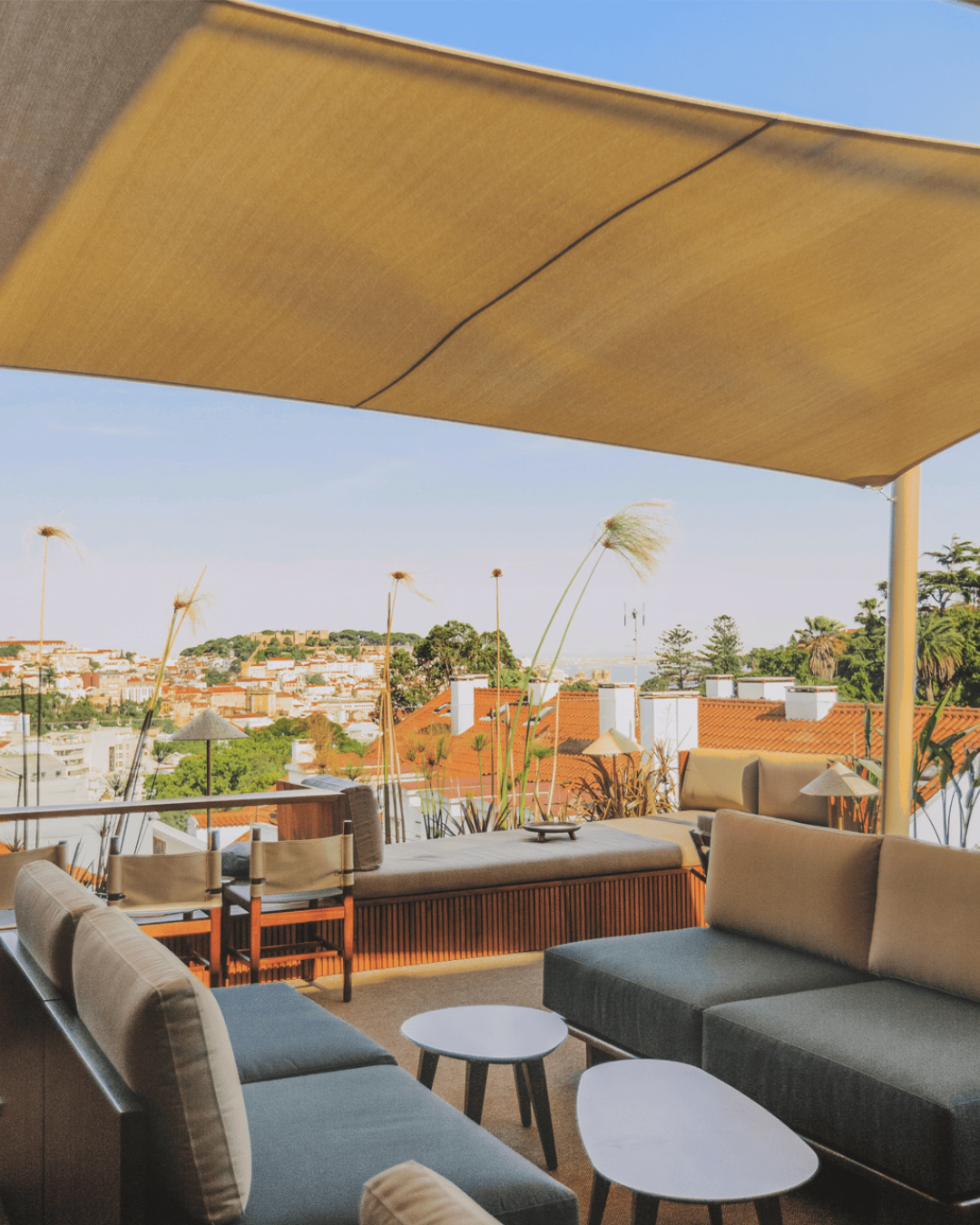 Stylish rooftop terrace at V Rooftop Bar, Lisbon, with shaded lounge seating and panoramic views over the city's terracotta rooftops towards the castle