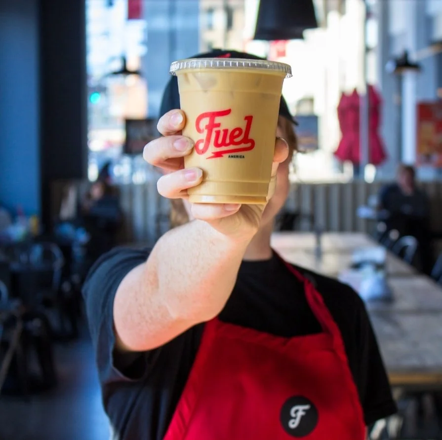 Fuel America Iced Coffee Held by Barista Inside Café