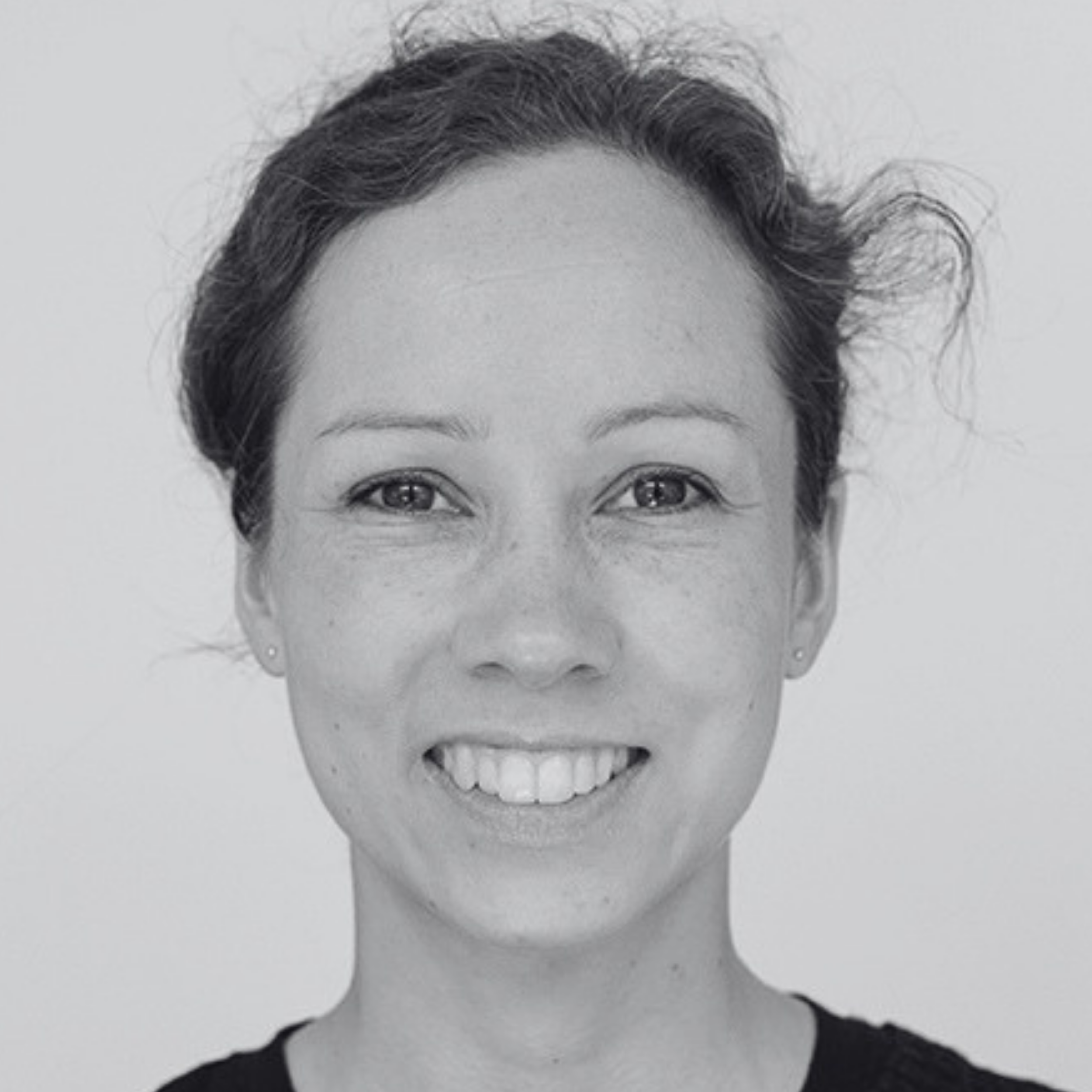 Black and white photo of a smiling woman with curly hair, wearing a dark top.