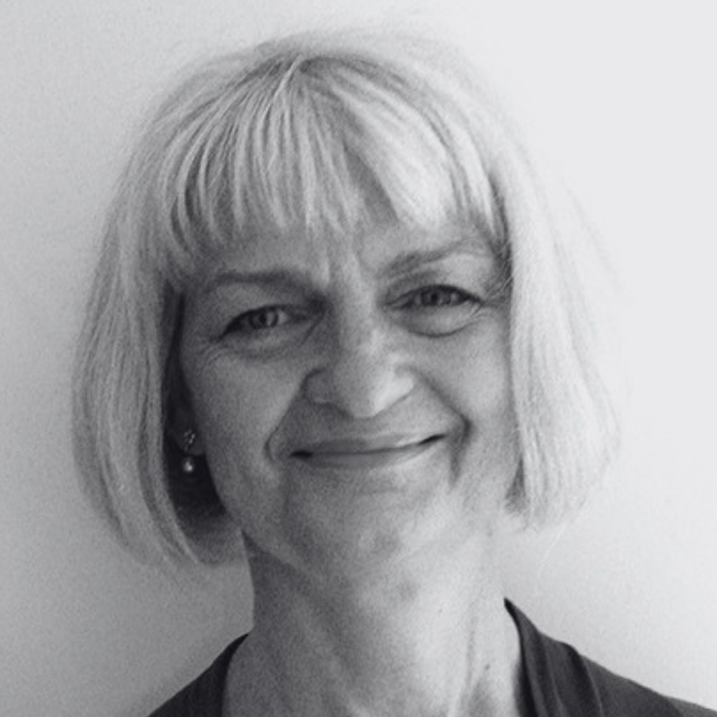 Black and white photograph of a smiling woman with short hair, wearing earrings and a dark top.