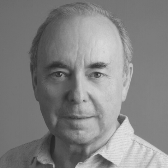 [Image Description: Black and white headshot of a man with short hair. Paul is wearing a button up shirt with a collar. He is smiling faintly at the camera.]
