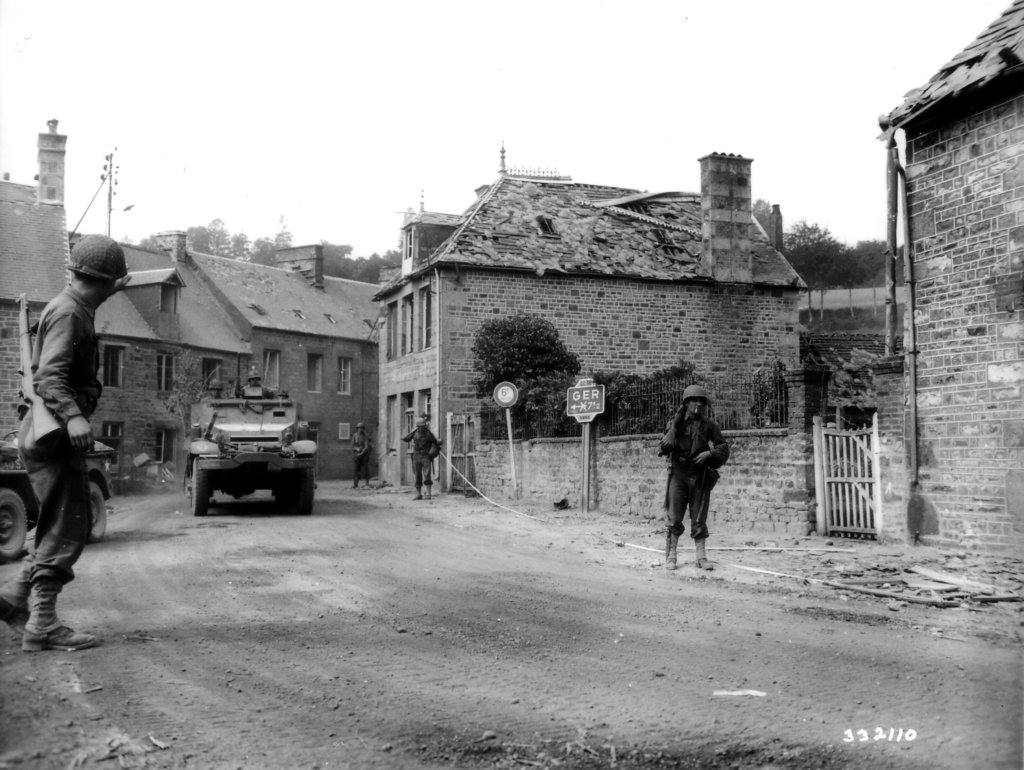 Infantry and a half-track of the 41st Armored Infantry Regiment enter the village of Lonlay L'Abbaye, France, 14th Aug 1944.