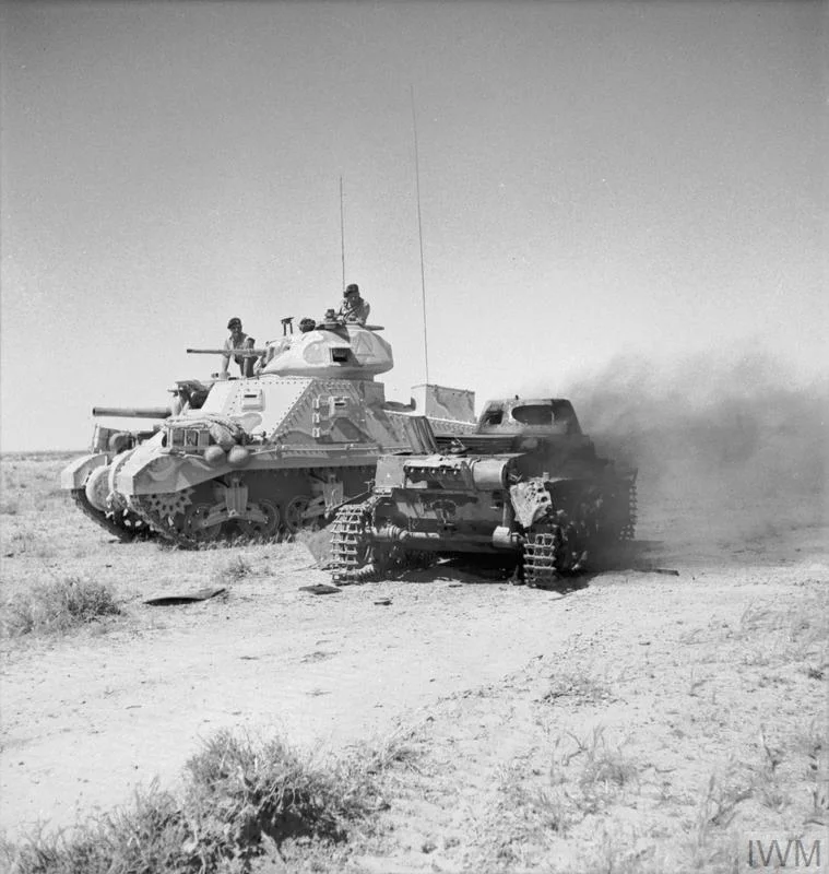 A Grant tank passes a burning German PzKpfw I tank, 6 Jun 1942. IWM photo E 12920