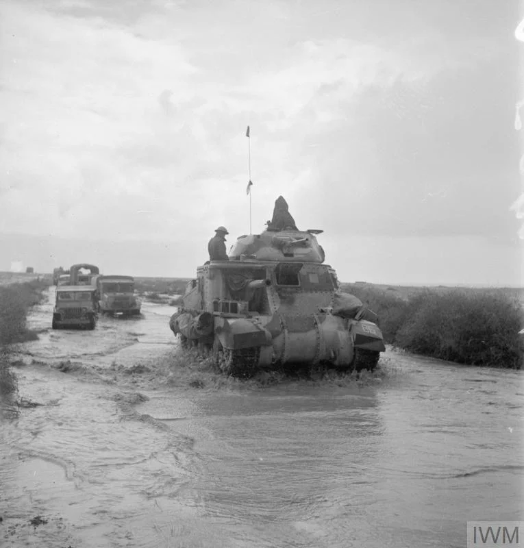 A Grant tank and trucks make their way along a road flooded by recent rains while in pursuit of the enemy, 10 Nov 1942. IWM photo E 19230