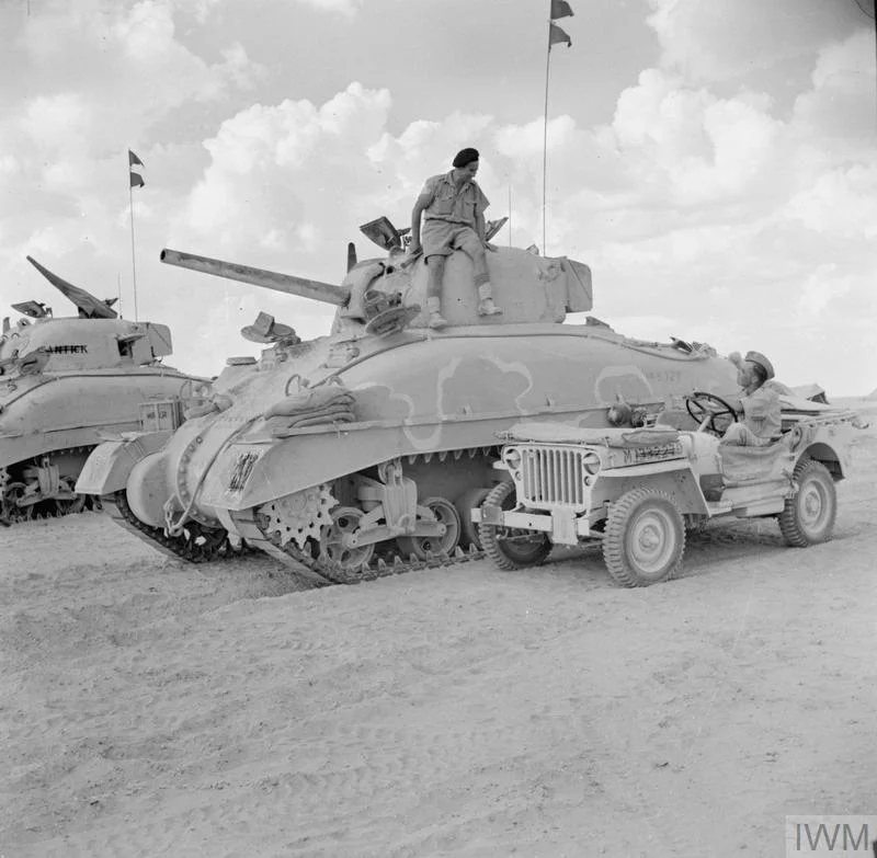 A jeep and Sherman tanks of HQ 2nd Armoured Brigade, 10 Oct 1942. "The white line on the tank was being used as a guideline by the Camouflage Unit who were called away before completing the painting of the Brigade's tanks." IWM photo E 17898.