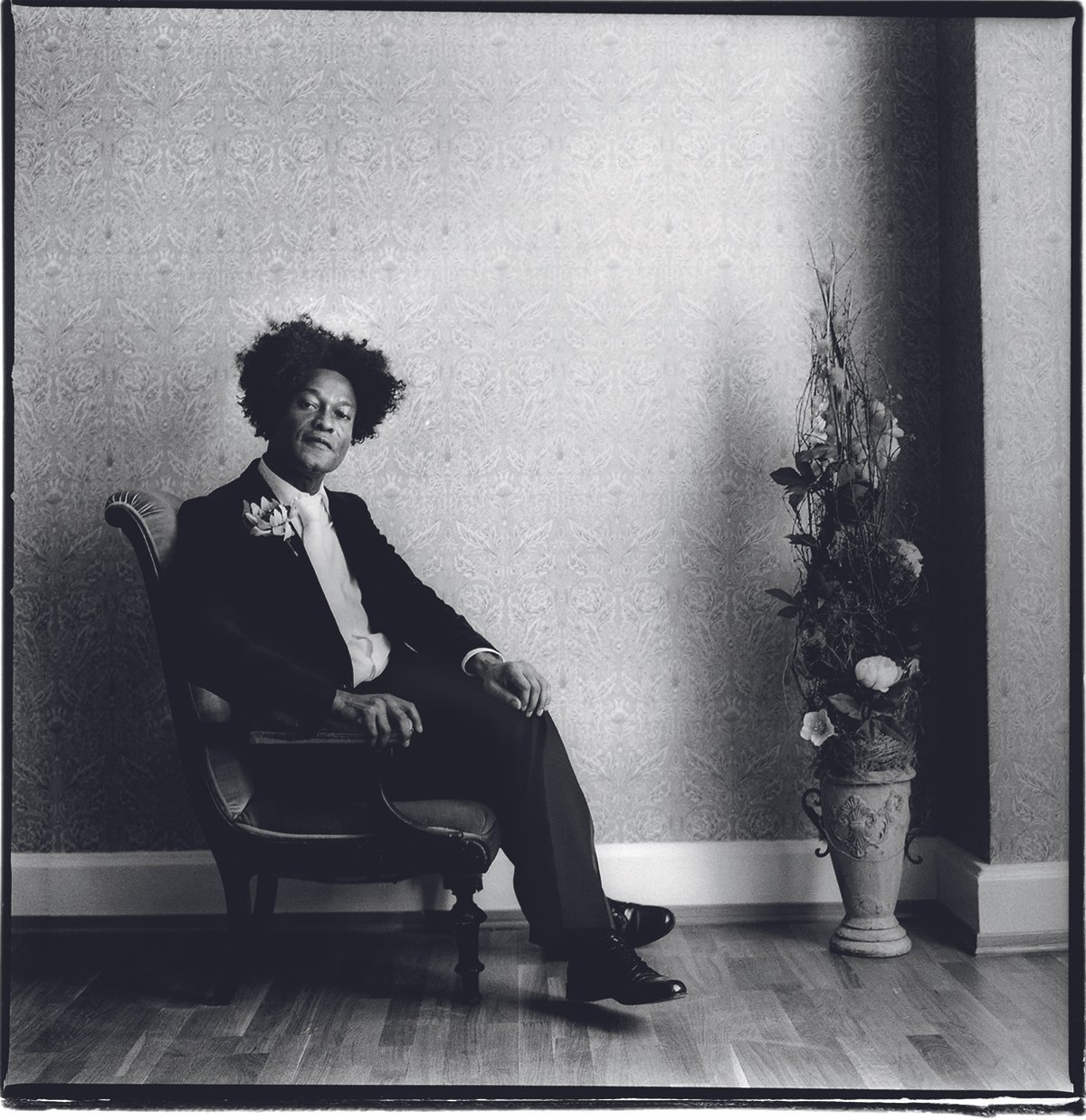 Ike Ude i en stol i et rom met en blomsteroppsats