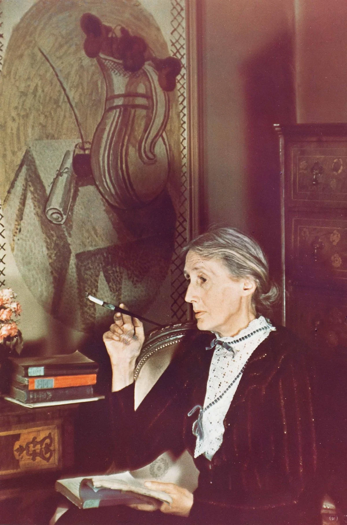 Virginia Woolf med bok og sigarett foran et bilde utført av Vanessa Bell