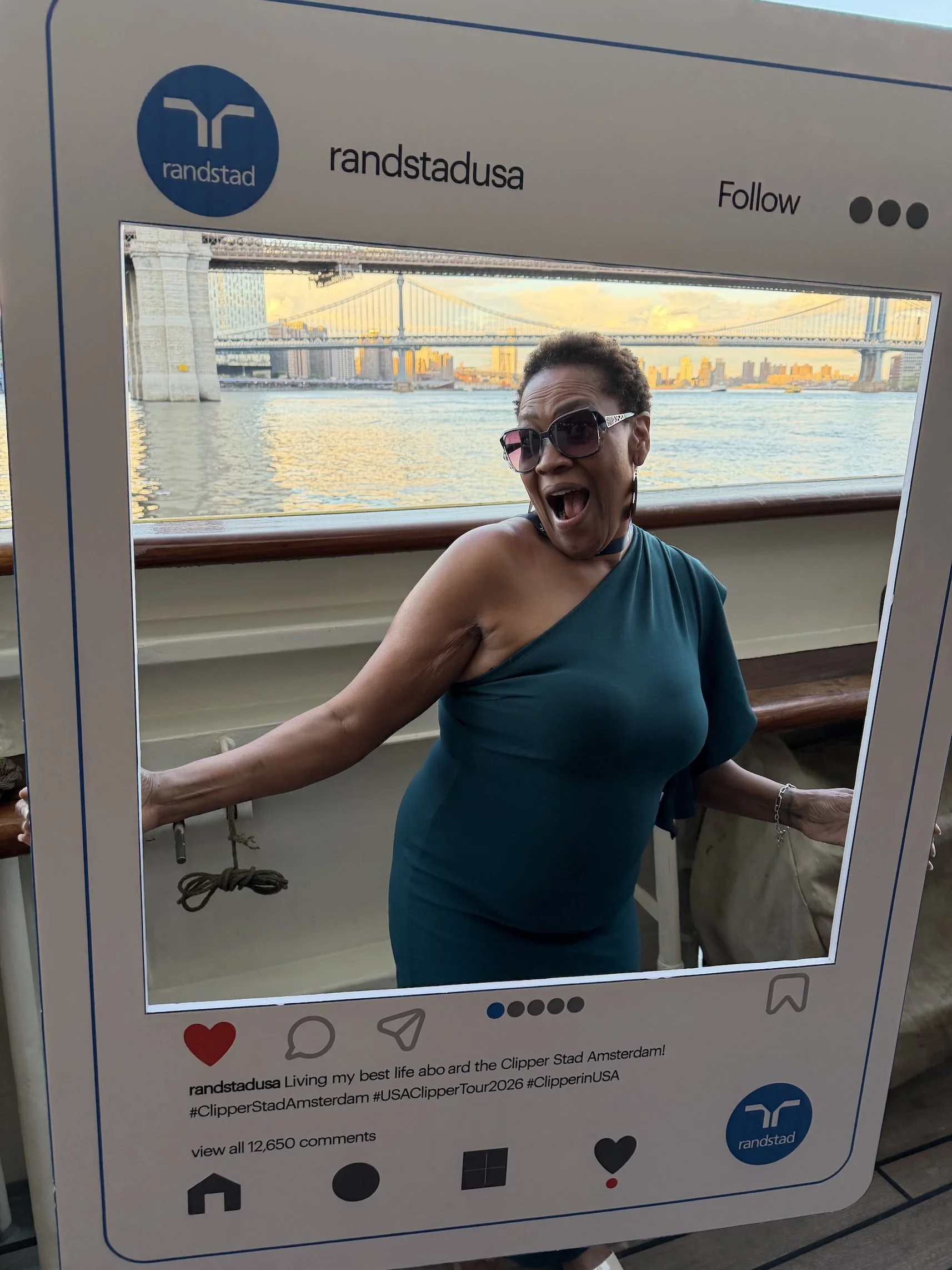 A woman in a teal dress and sunglasses smiling and posing inside a photo frame designed to look like an Instagram post, with a cityscape and bridge visible through a window behind her.