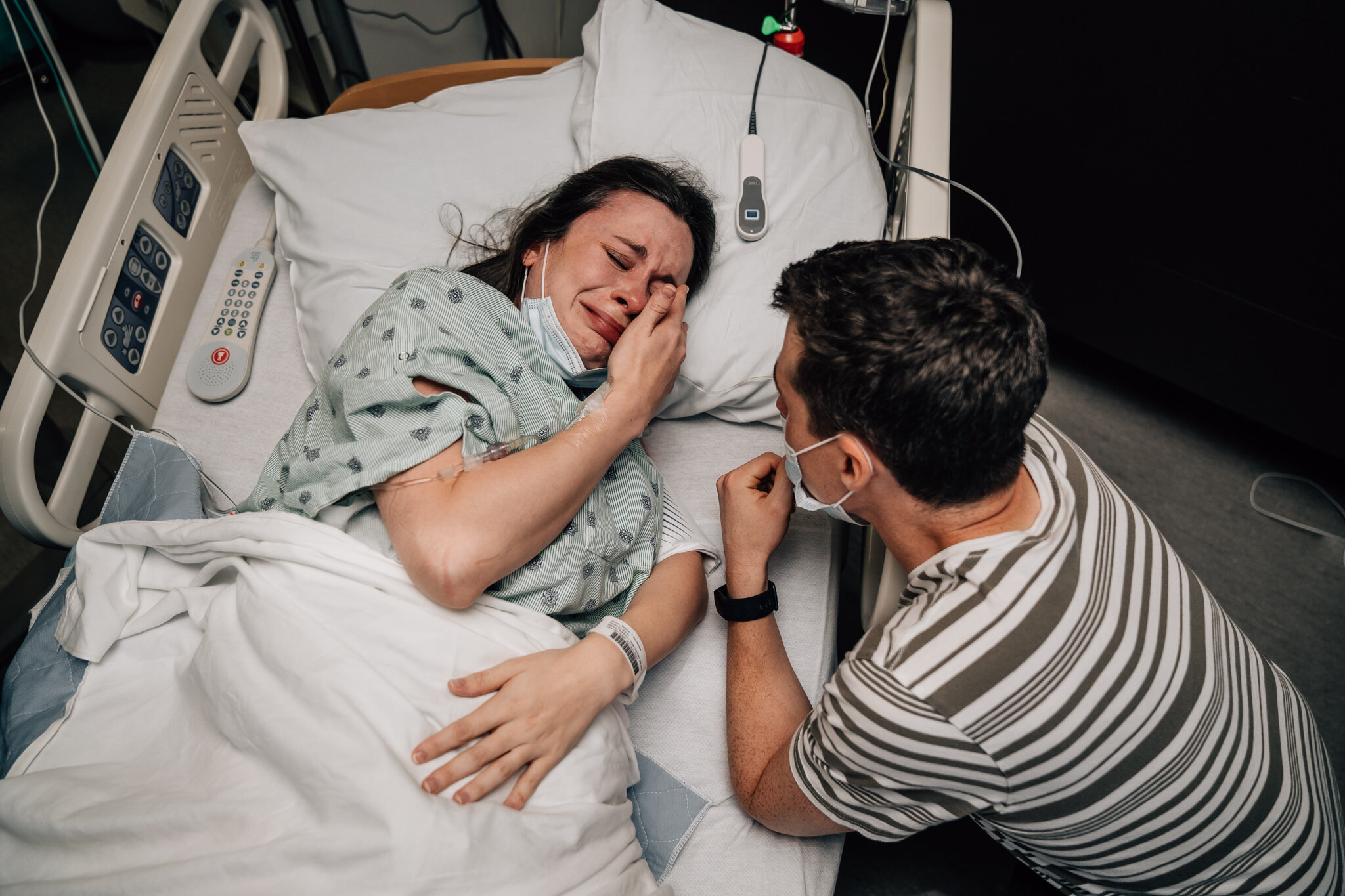 Supported by her husband, a birthing person in a hospital bed cries with joy at the news that she is ready to push and about to get her VBAC.