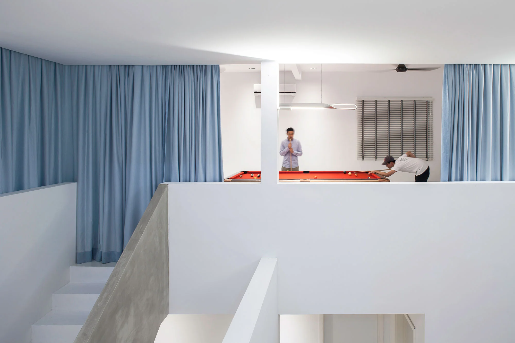 A simple interior finishes palette of white washed walls, exposed cement, and wood grained floor tiles makes for easy maintenance. A blue color group of curtains wraps the entire 3 level of the atrium to provide visual privacy and flexibility to the use of the spaces.