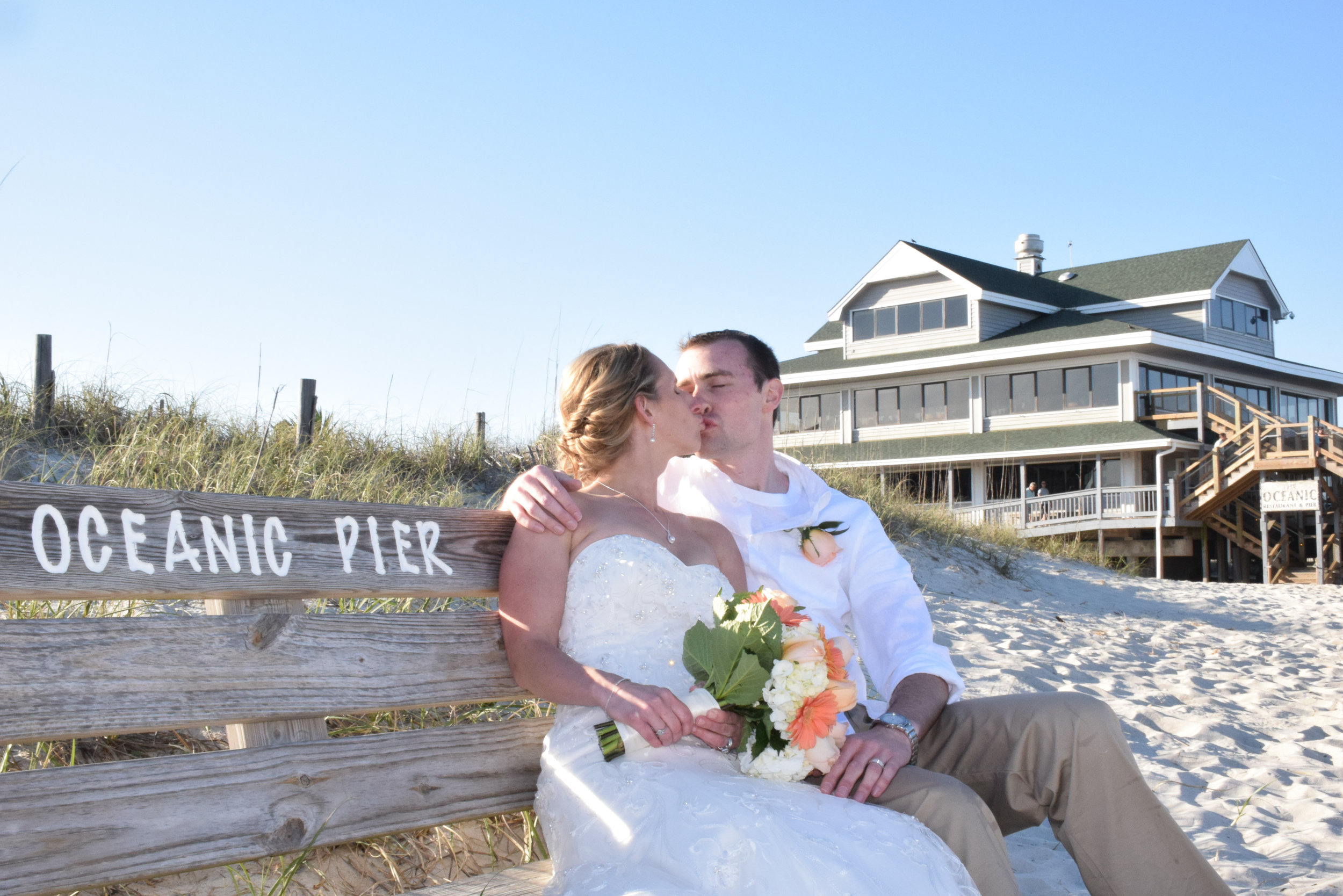Newly married couple kissing on bench.