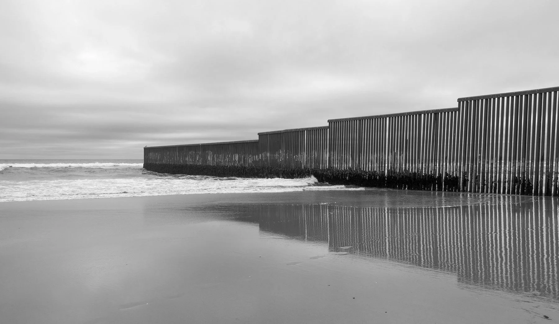 The border fence trails off into the Pacific Ocean.