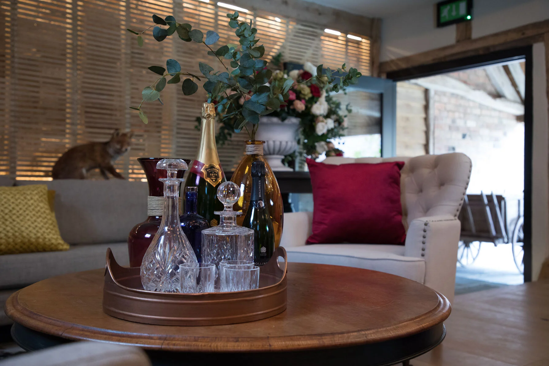 Crystal decanters and champagne bottles displayed on a tray in the centre of a round table, surrounded by cream armchairs