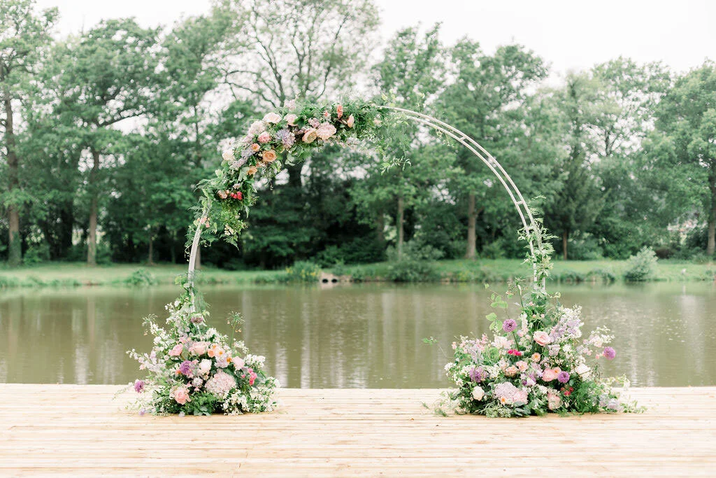 Romantic outdoor ceremony styling surrounded by seasonal flowers and natural greenery. Large archway with floral displays at each foot